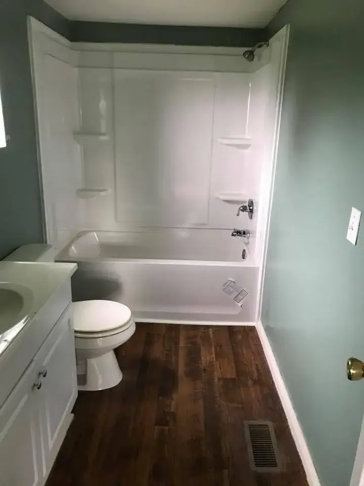 Finished bathroom with a white tub surround, white vanity and dark wood-look floor
