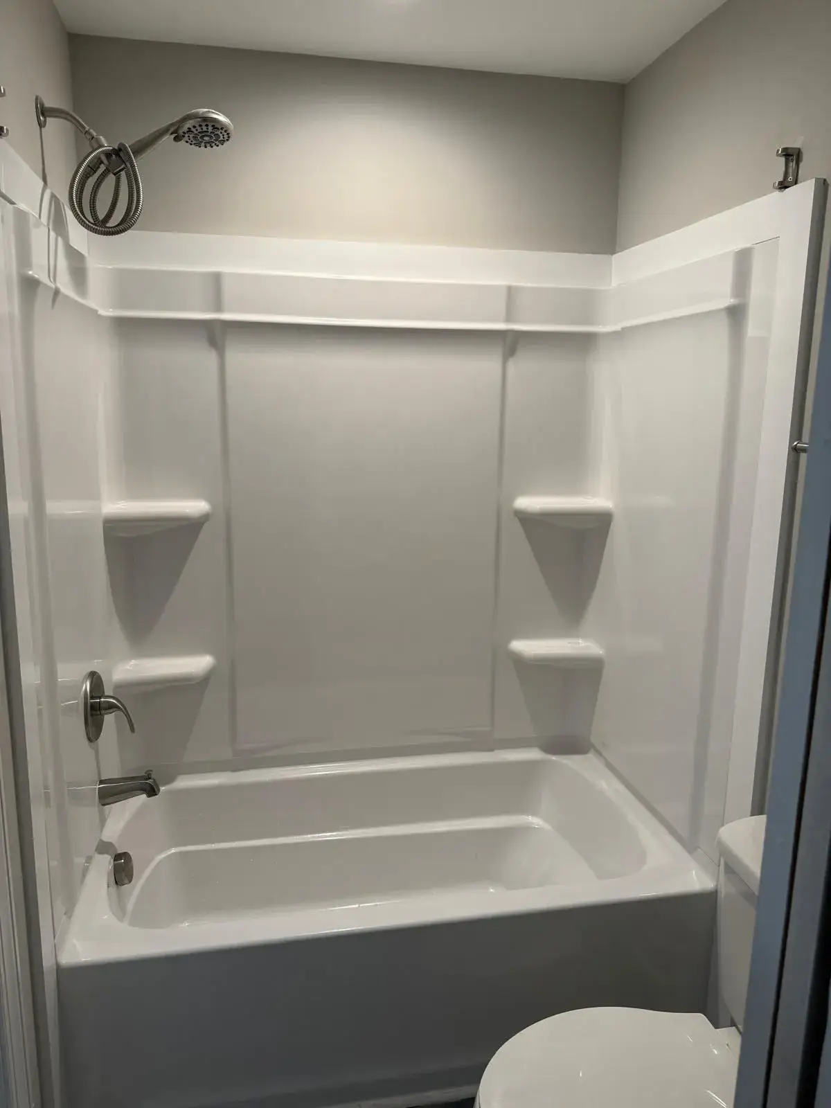New white tub and shower surround with a chrome shower head