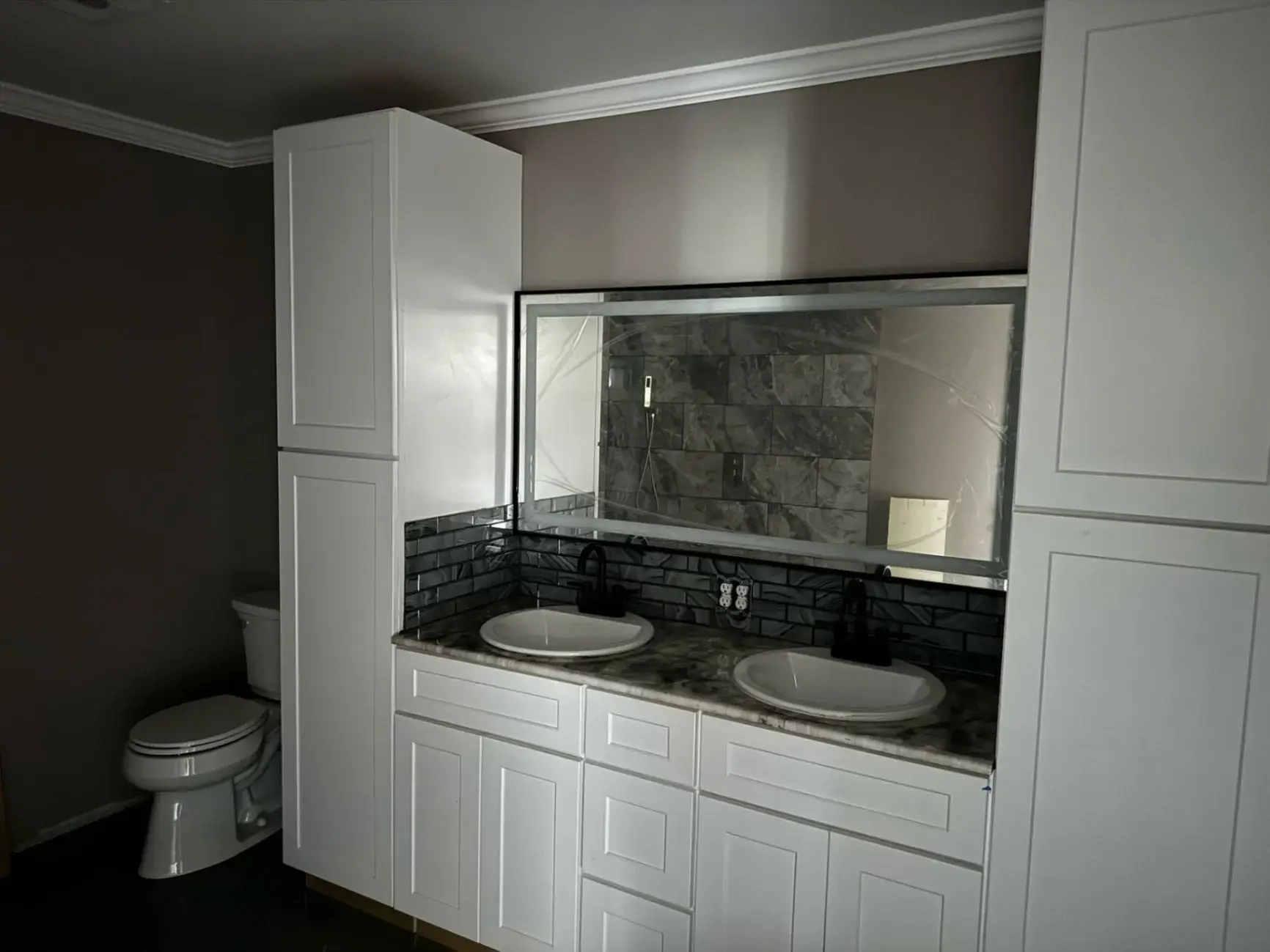Double vanity with white cabinets, dark tile and a framed mirror