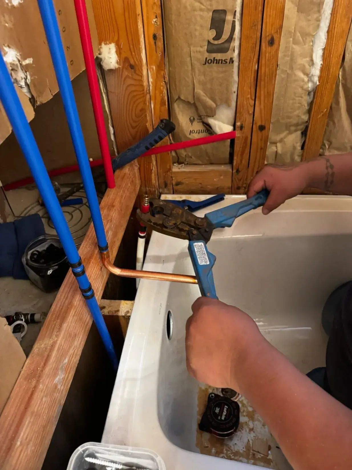 Crew member crimping new PEX water lines above a tub