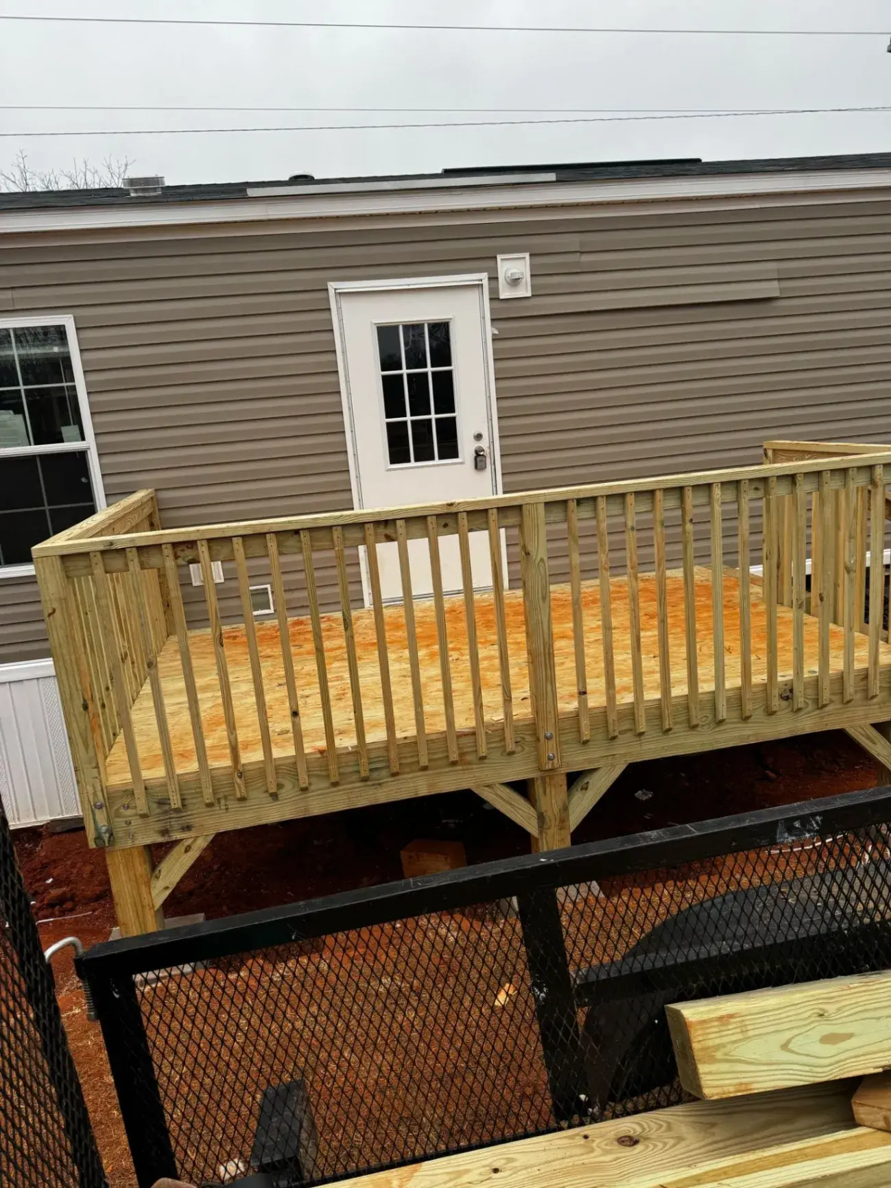 Pressure-treated deck and railing behind a gray home