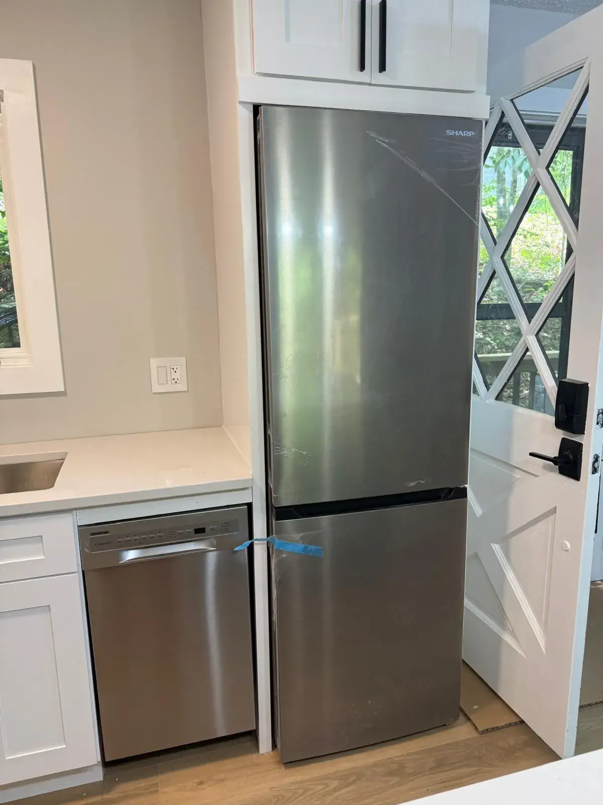 Stainless refrigerator and dishwasher set into new white cabinets
