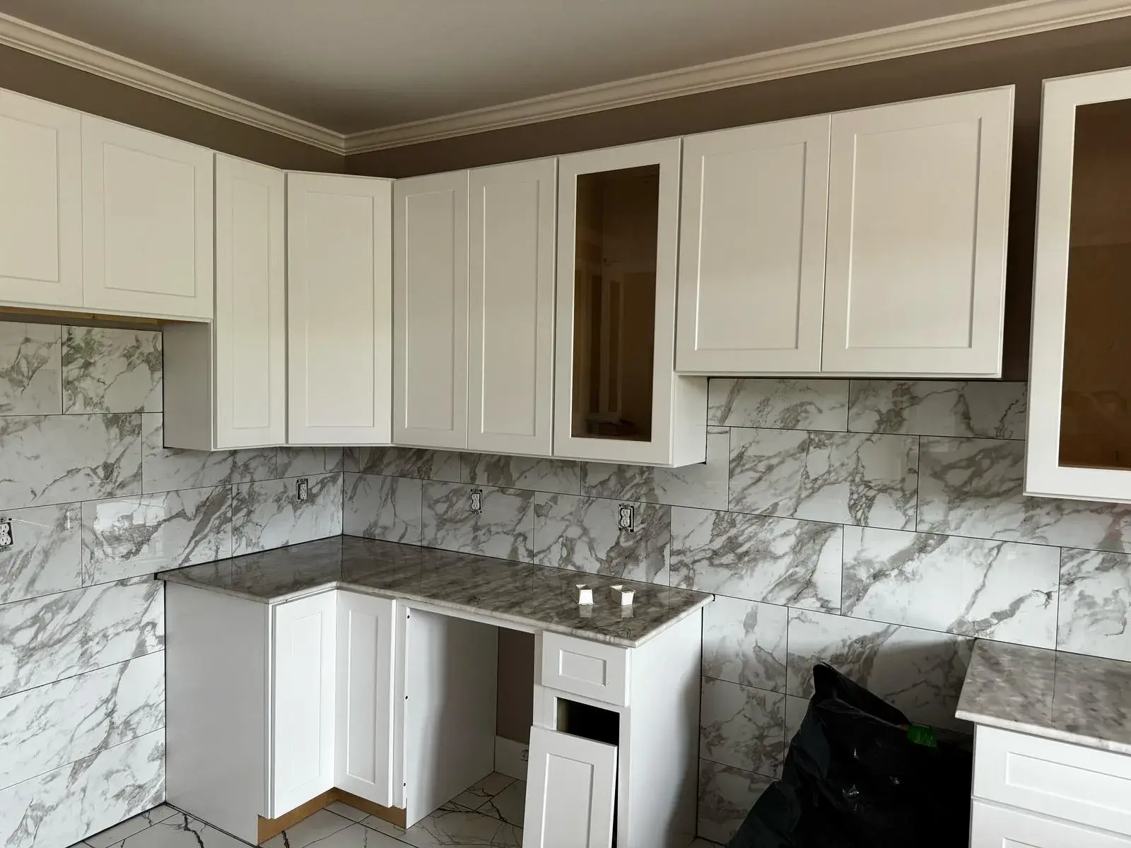 White cabinets with a glass door and marble-look tile backsplash