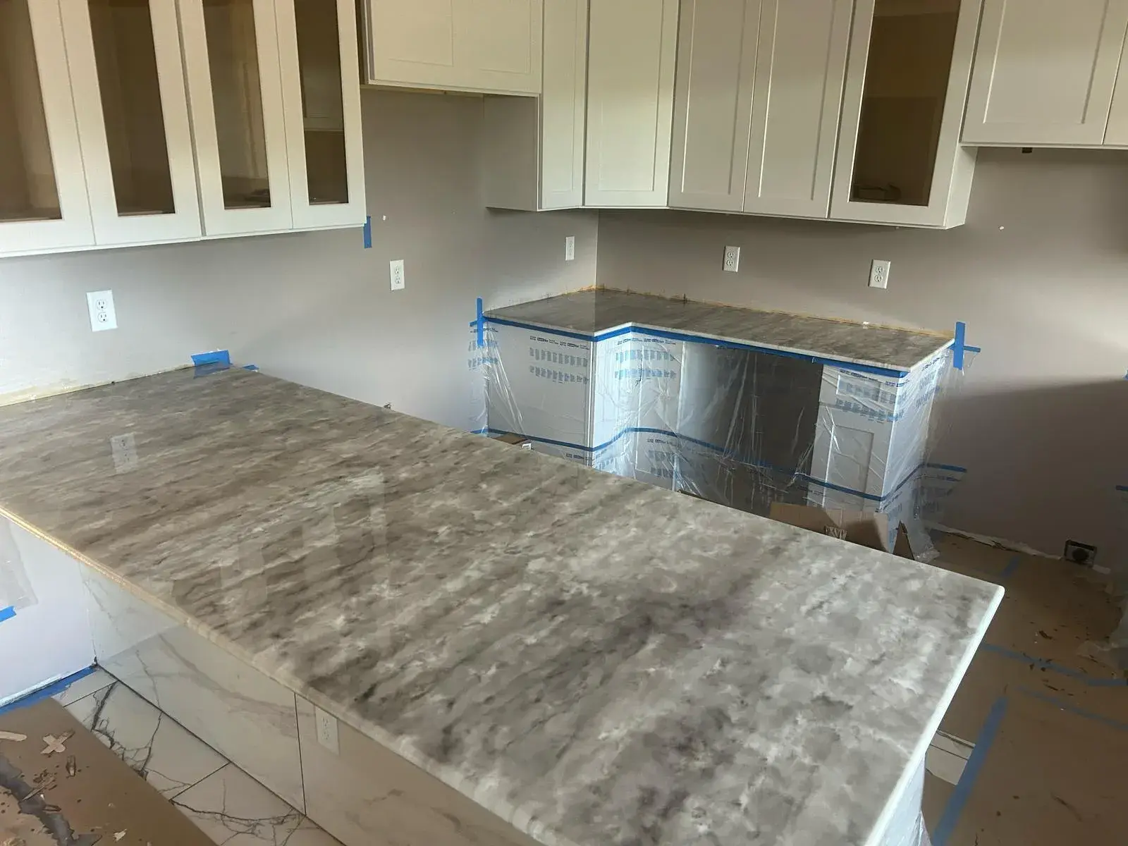 Marble-look countertop being fitted, with protective tape still on the cabinets