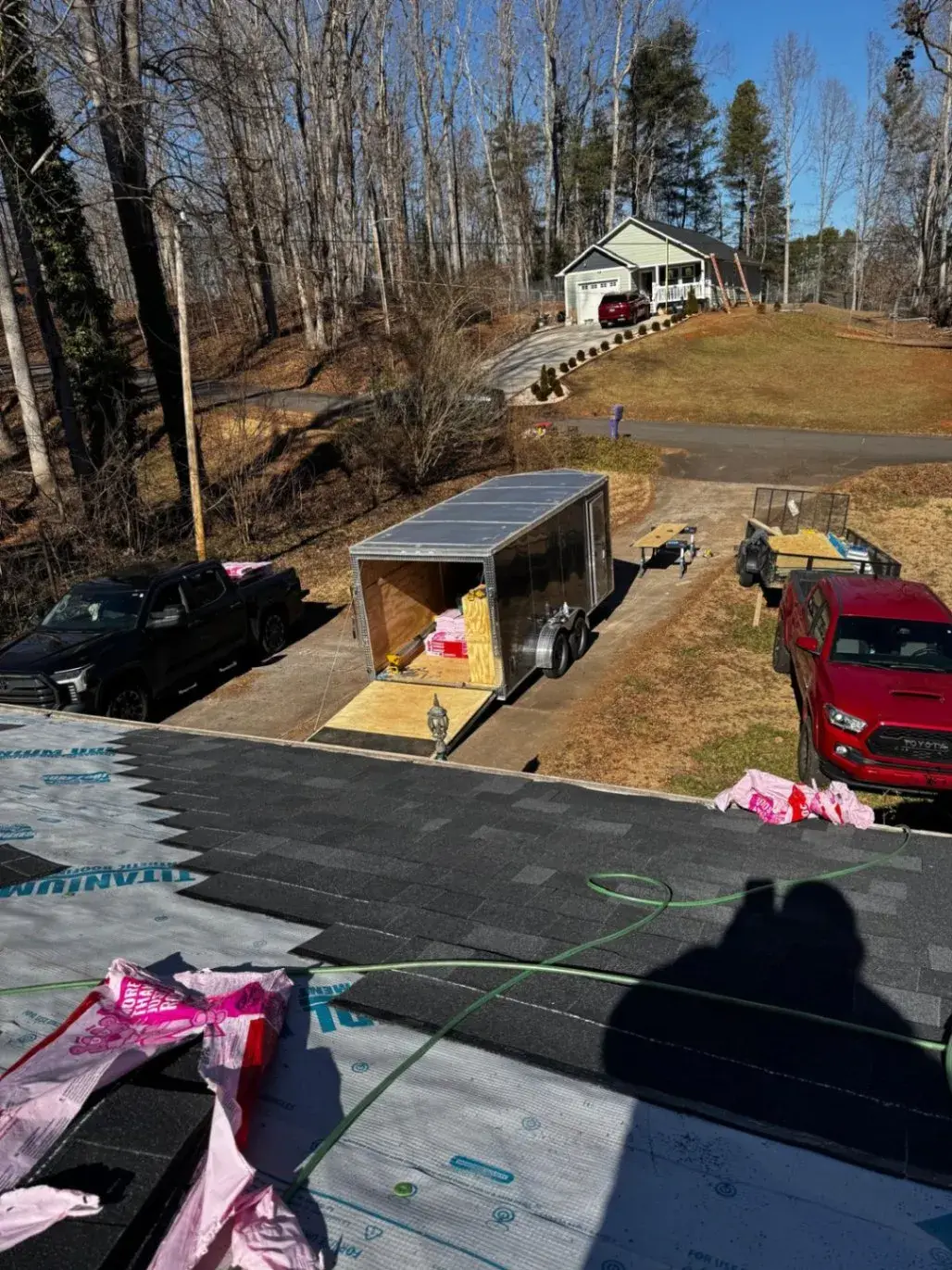 View from a roof during shingle installation, with the work trailer in the driveway below